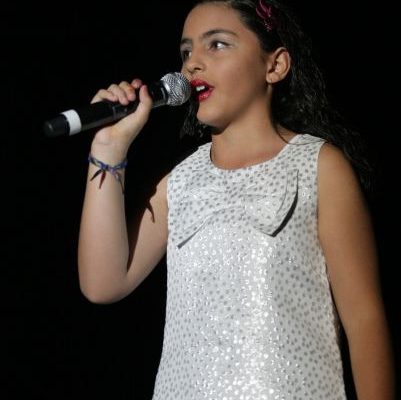 A young girl holds a microphone and sings into it.