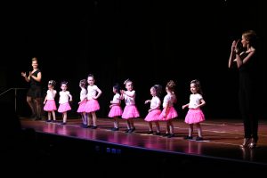 9 pre-school aged girls in pink skirts dacing with two teachers dressed in black