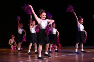 Young girls dressed as cheerleaders dance for an audience