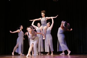 A graceful classical ballet performance by seven teenage girls with one girl on the shoulders of two others