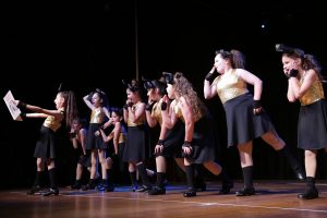 A large number of young girls in black and gold dance